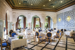 A dining area with tables set for multiple guests, featuring a patterned floor and ornate ceiling.