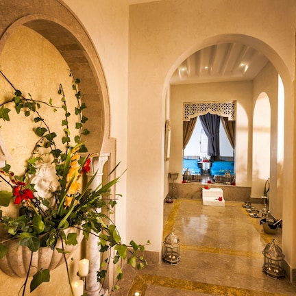 An arched hallway with a floral arrangement, candle holders, and a view into a room with a bed and a window.