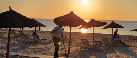 A beach with sun umbrellas, lounge chairs, and a person walking.