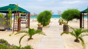 Ein Strandweg, der zu Strandliegen und Sonnenschirmen führt.