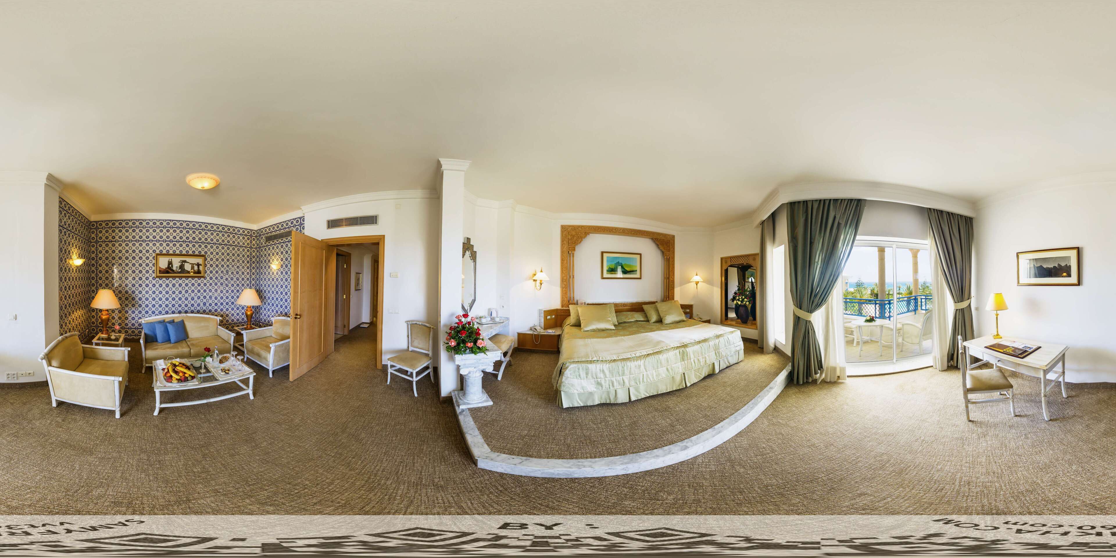 Amplia habitación de hotel con una cama grande, zona de estar con sofá y sillones, mesa de comedor y vistas al exterior.