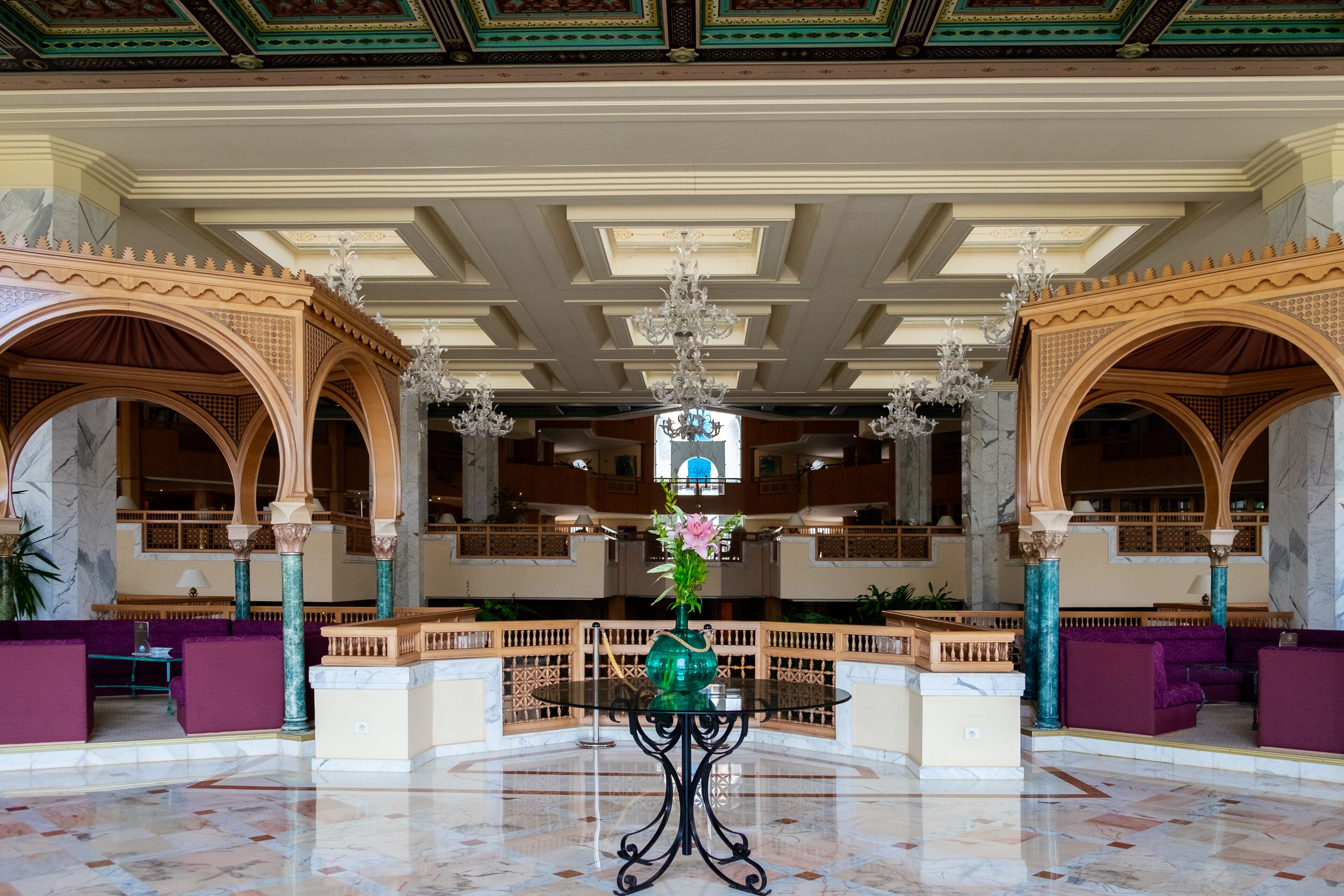 A grand lobby with marble floors, ornate columns, and a central table with a vase of flowers.