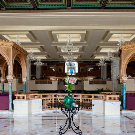 A grand lobby with marble floors, ornate columns, and a central table with a vase of flowers.