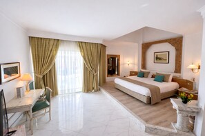 Una habitación de hotel con una cama grande, un escritorio con una silla, una lámpara de escritorio y un ventanal con cortinas.