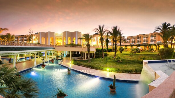 Ein Hotelpoolbereich mit mehreren Pools, Palmen und einem überdachten Gang.