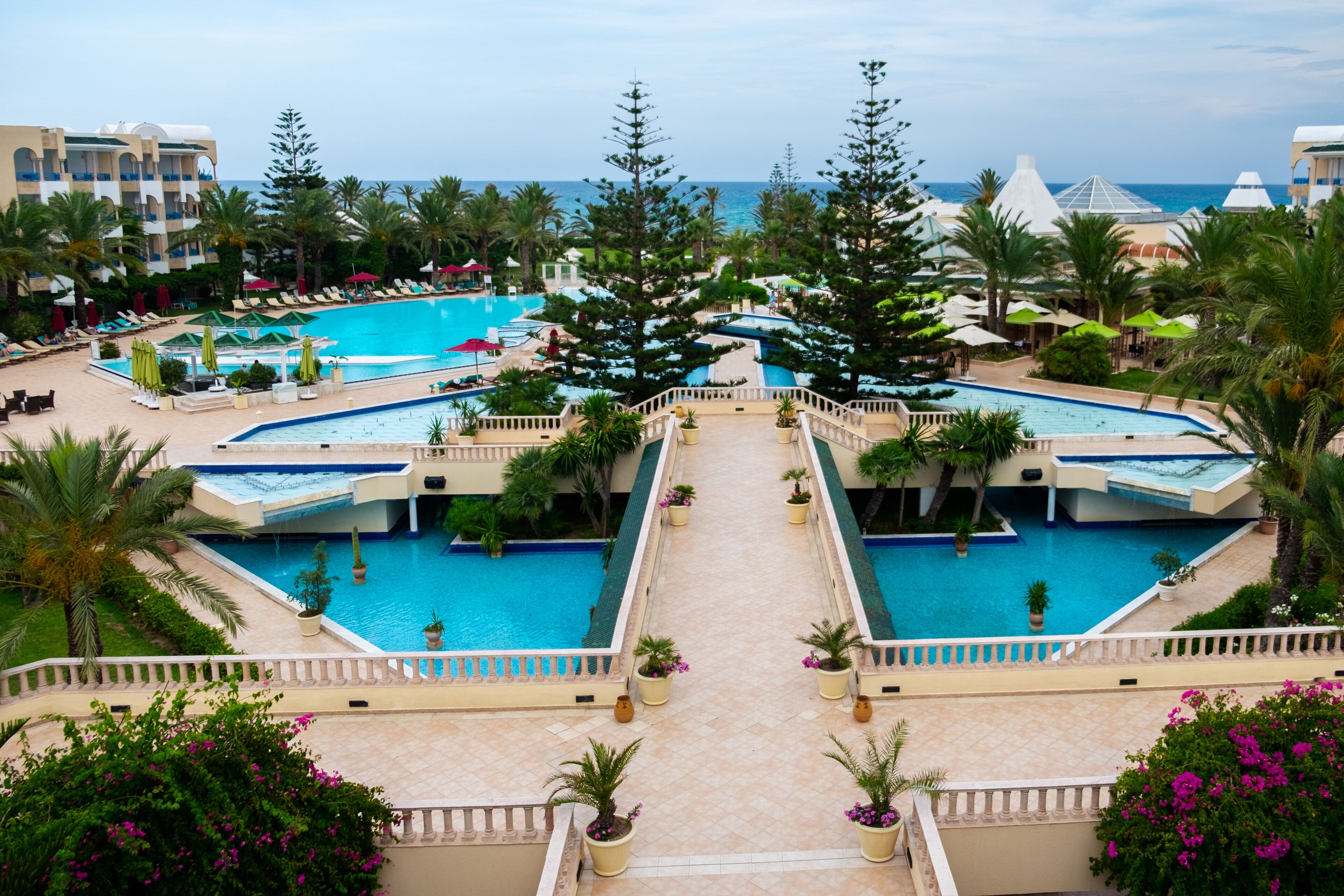 A resort with multiple swimming pools, palm trees, and a view of the ocean.