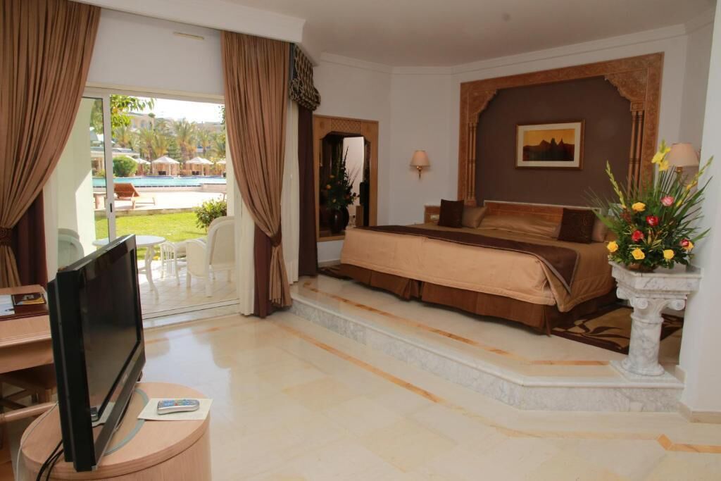 Habitación de hotel con cama, televisión, escritorio y vista a una piscina.
