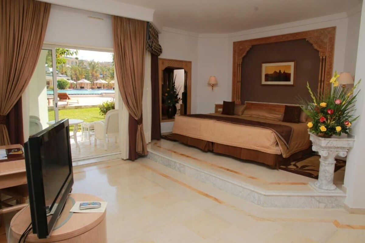 Habitación de hotel con cama, televisión, escritorio y vista a una piscina.