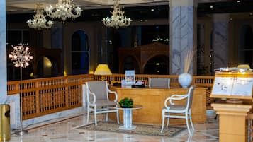 Un vestíbulo con mostrador de recepción, sillas blancas, candelabros y suelo de mármol.