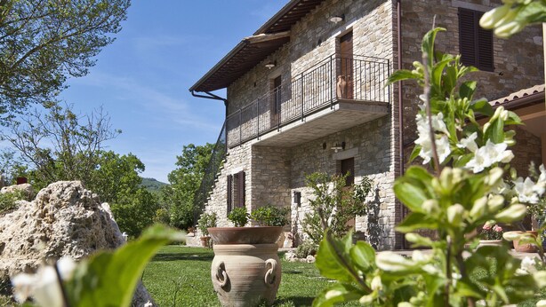 A stone building with a balcony, surrounded by greenery and a large pot. - Relais Parco del Subasio (Assisi)
