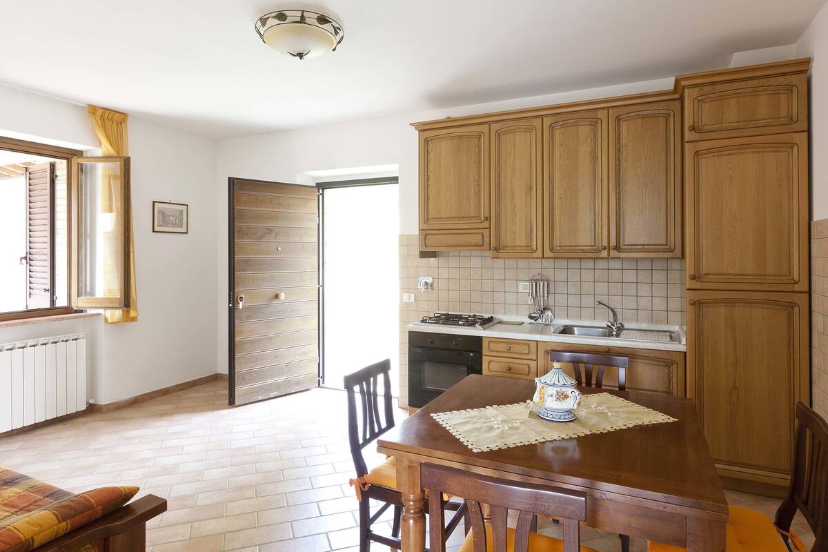 A kitchen with wooden cabinets, a dining table with chairs, a window with curtains, and a radiator.