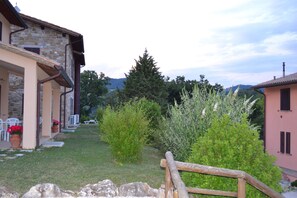 Un edificio de piedra con jardín, una cerca de madera y vistas del paisaje circundante.