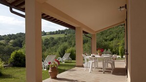 A covered patio with a table and chairs, overlooking a lush green landscape. - Relais Parco del Subasio (Assisi)