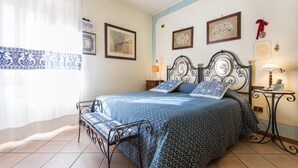 Un dormitorio con cama, una silla, una mesita de noche y una pared decorada con cuadros.