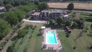 An aerial view of a large villa with a swimming pool, surrounded by lush greenery and a hilly landscape.