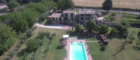An aerial view of a large villa with a swimming pool, surrounded by lush greenery and a hilly landscape.