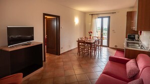 A living room with a TV, a red sofa, a dining area with chairs, and a kitchen with a microwave.