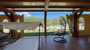 An outdoor seating area with a table and chairs, a hanging chair, and a view of a pool and greenery.