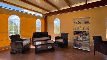 Una habitación con muebles de mimbre, ventanas amplias y una vitrina de cristal con objetos.
