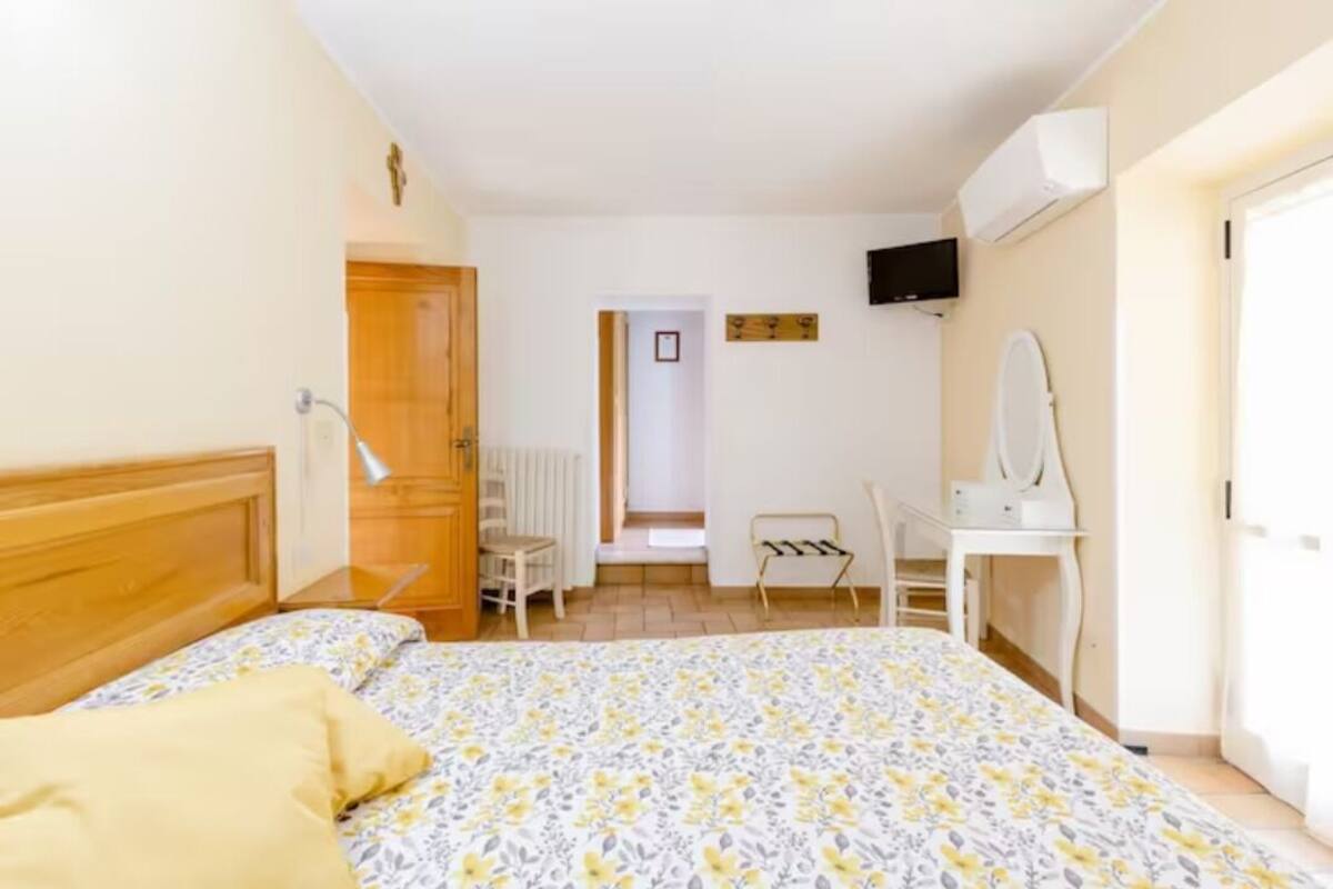 A bedroom with a bed, a desk, a chair, a mirror, and a television on the wall.
