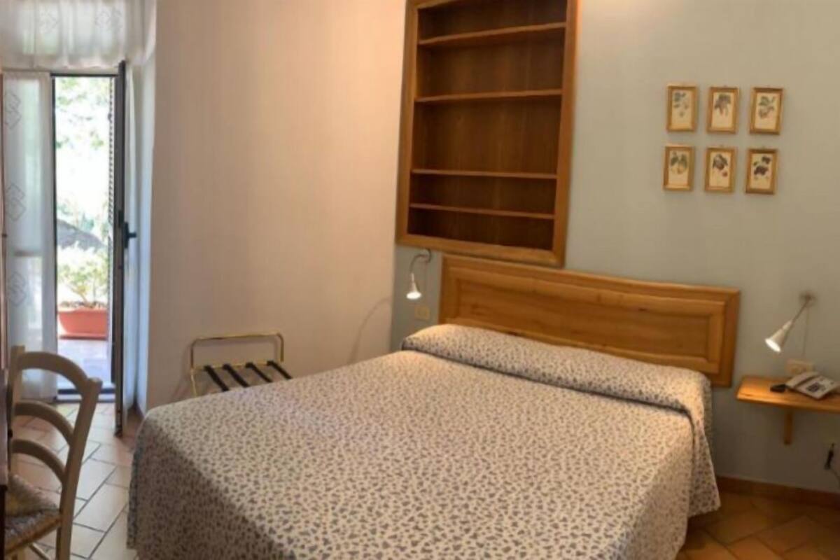 A bedroom with a bed, a wooden headboard, a desk, and a chair. There is a window with a view of the outside.