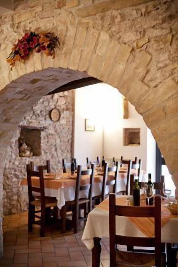 A stone archway leading to a dining area with tables and chairs, and a rustic stone wall.