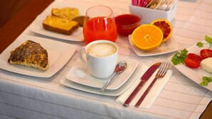 A breakfast setting with toast, a glass of orange juice, a cup of coffee, and a plate with tomatoes and a slice of orange.