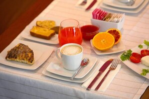 Una colazione con pane tostato, un bicchiere di succo d'arancia, una tazza di caffè e un piatto con pomodori e una fetta d'arancia.