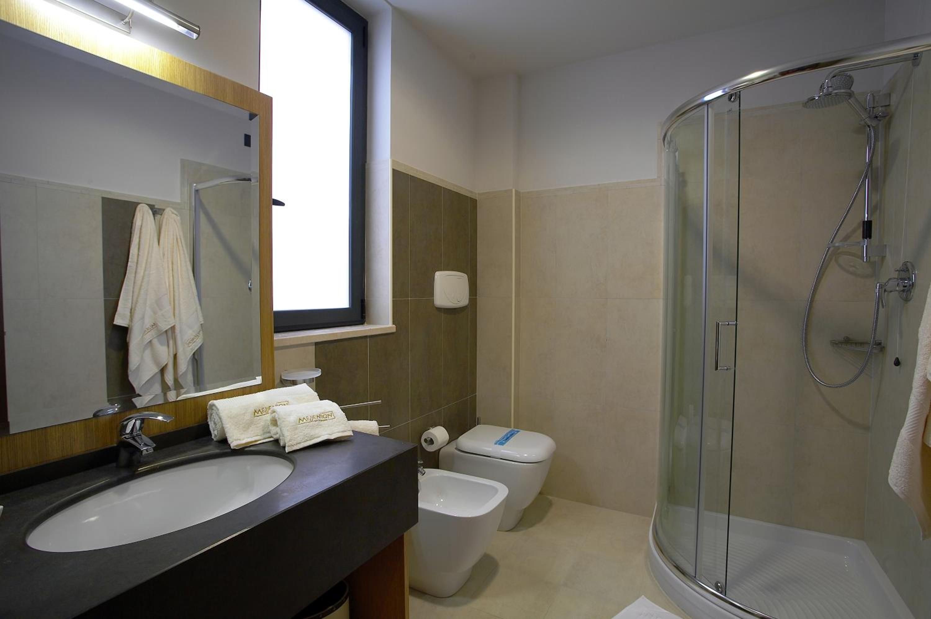 Casa de banho com lavatório, sanita, bidé e cabine de duche com parede de vidro.