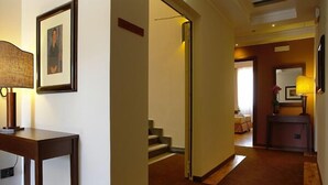 A hotel hallway with a wooden table, framed artwork, and a staircase leading to another room.
