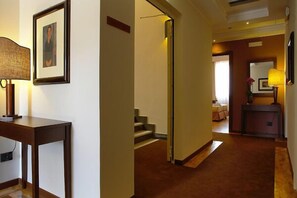 Un corridoio d'hotel con un tavolo in legno, opere d'arte incorniciate e una scala che conduce a un'altra stanza.
