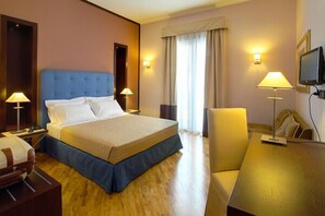 Una camera d'albergo con un letto grande, lampade sui comodini, una scrivania e un televisore.