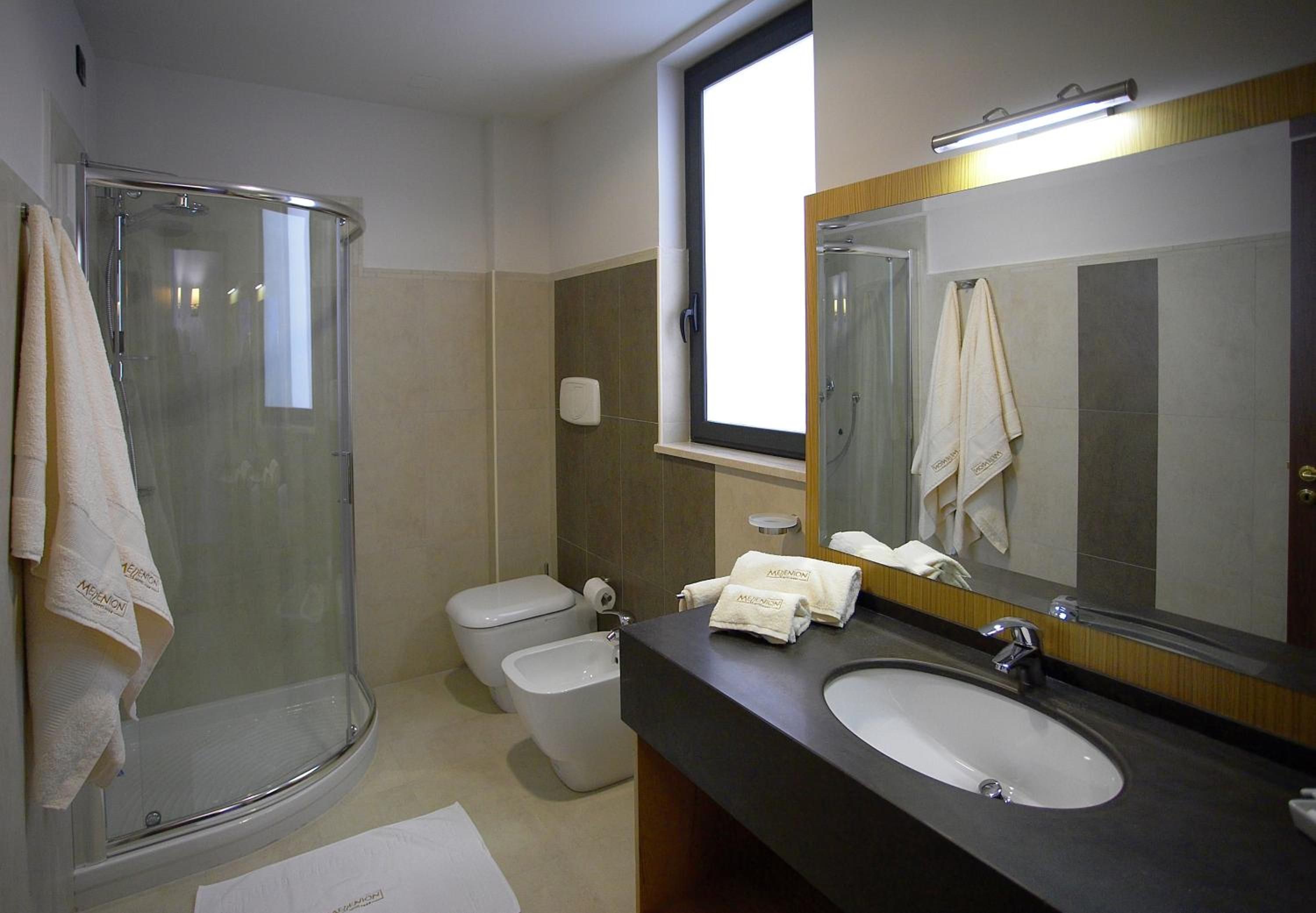 Un bagno con doccia vetro-muraria, un WC, un bidet e un lavandino con specchio.