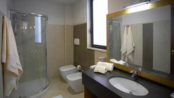 Un bagno con doccia vetro-muraria, un WC, un bidet e un lavandino con specchio.