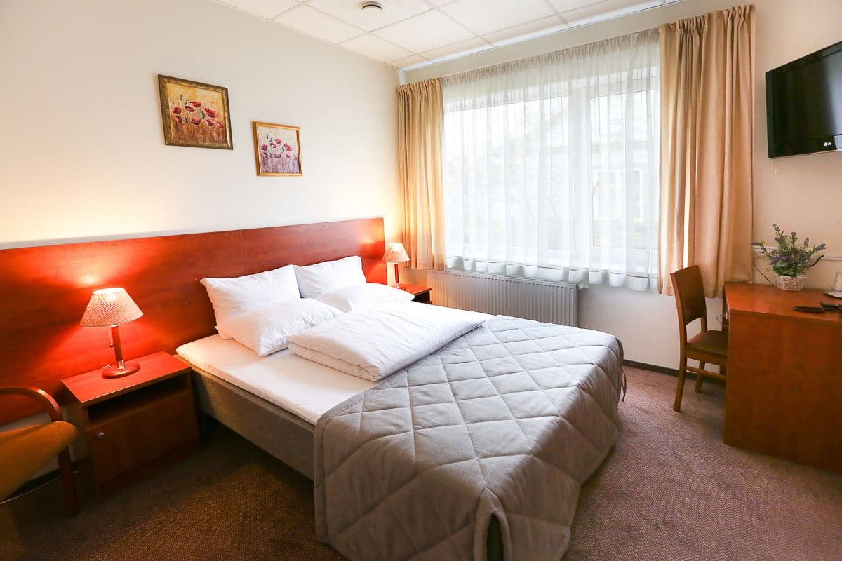 Habitación de hotel con cama, escritorio, silla, televisión y dos cuadros en la pared.