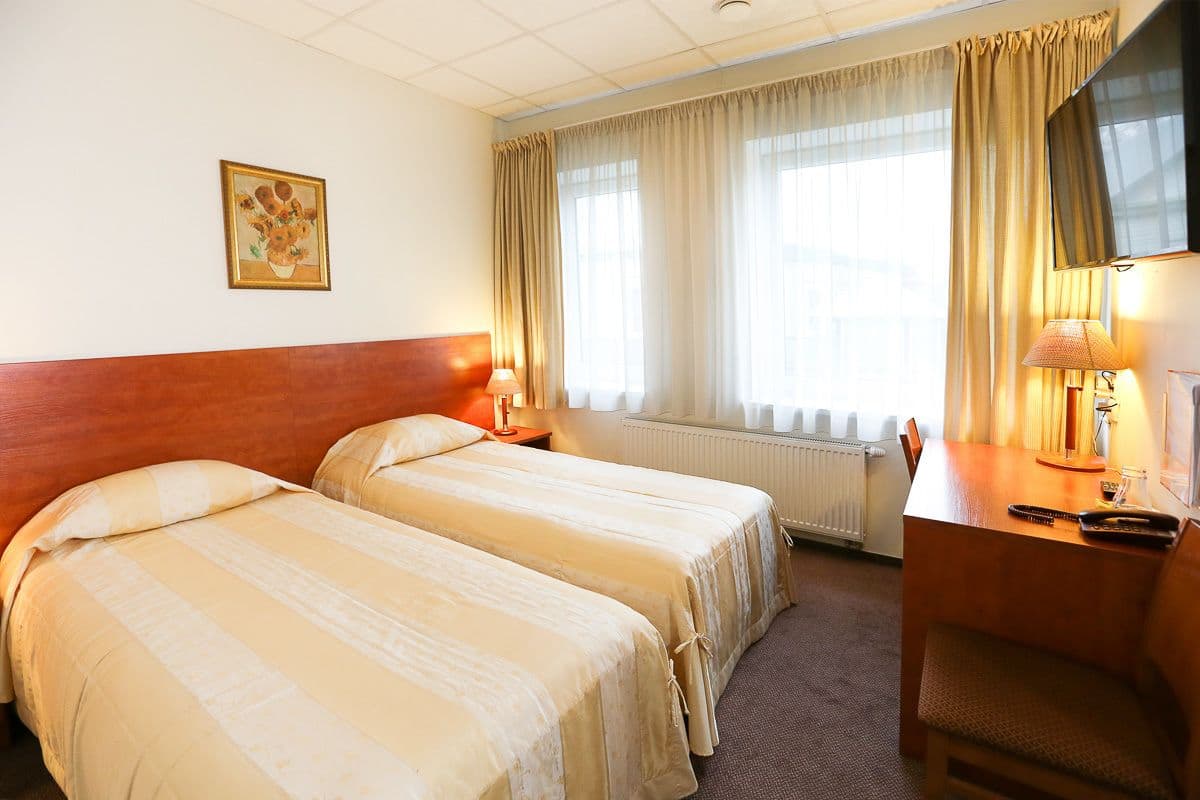 Habitación de hotel con dos camas, cabecero de madera, un escritorio con silla, televisor y ventana con cortinas.