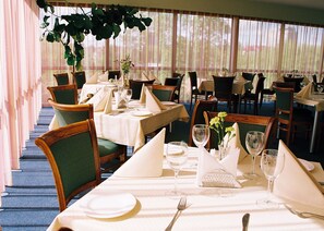 A restaurant with multiple tables set for dining, featuring green upholstered chairs and white tablecloths.