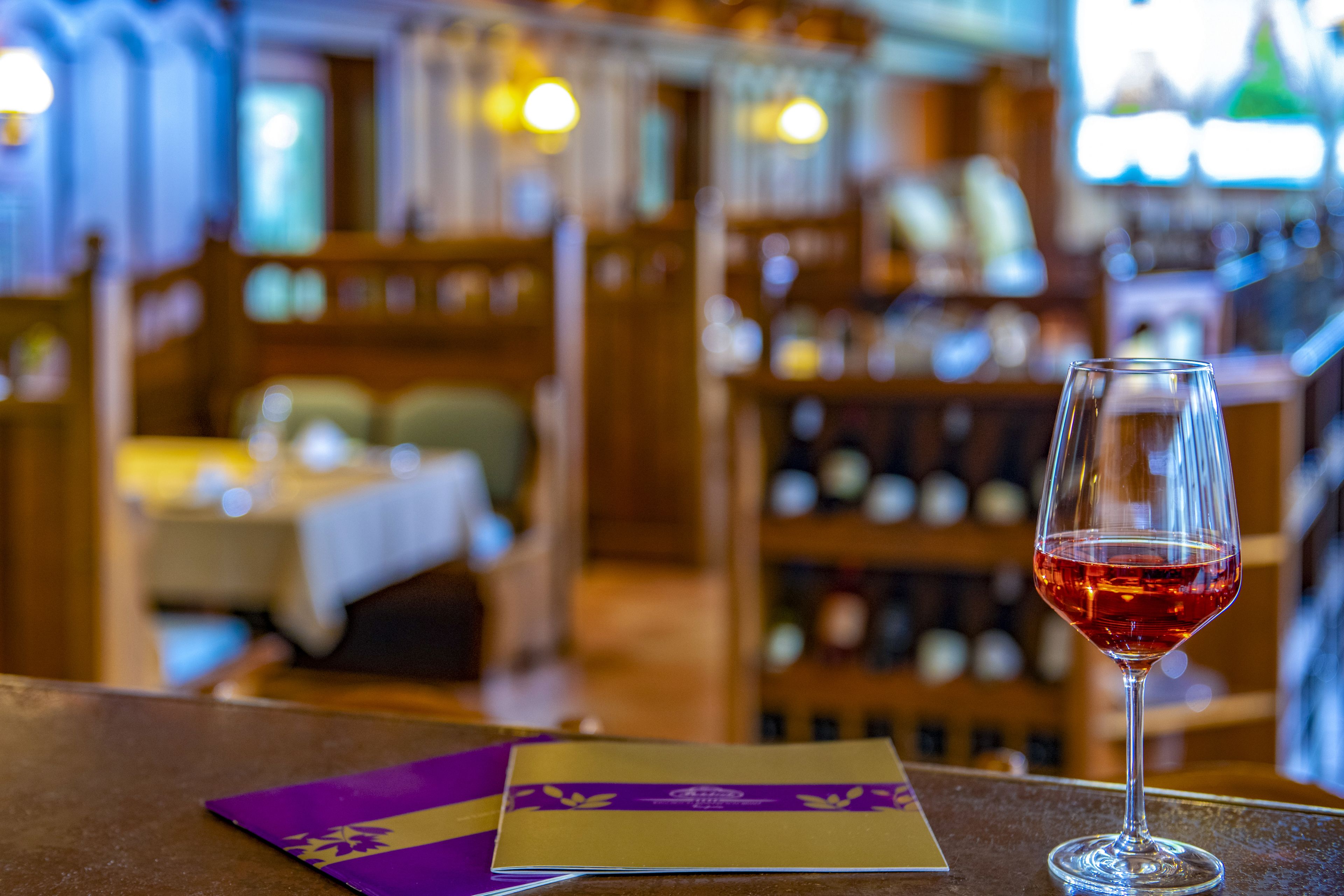 Angolo bar con un bicchiere di vino rosso, un menu e una cantina sullo sfondo.