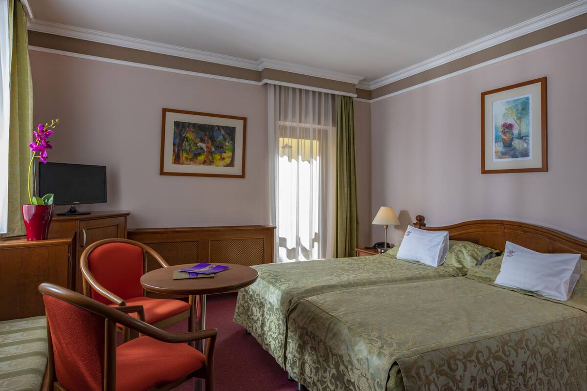 A hotel room with a bed, a desk, a chair, a television, and artwork on the walls.