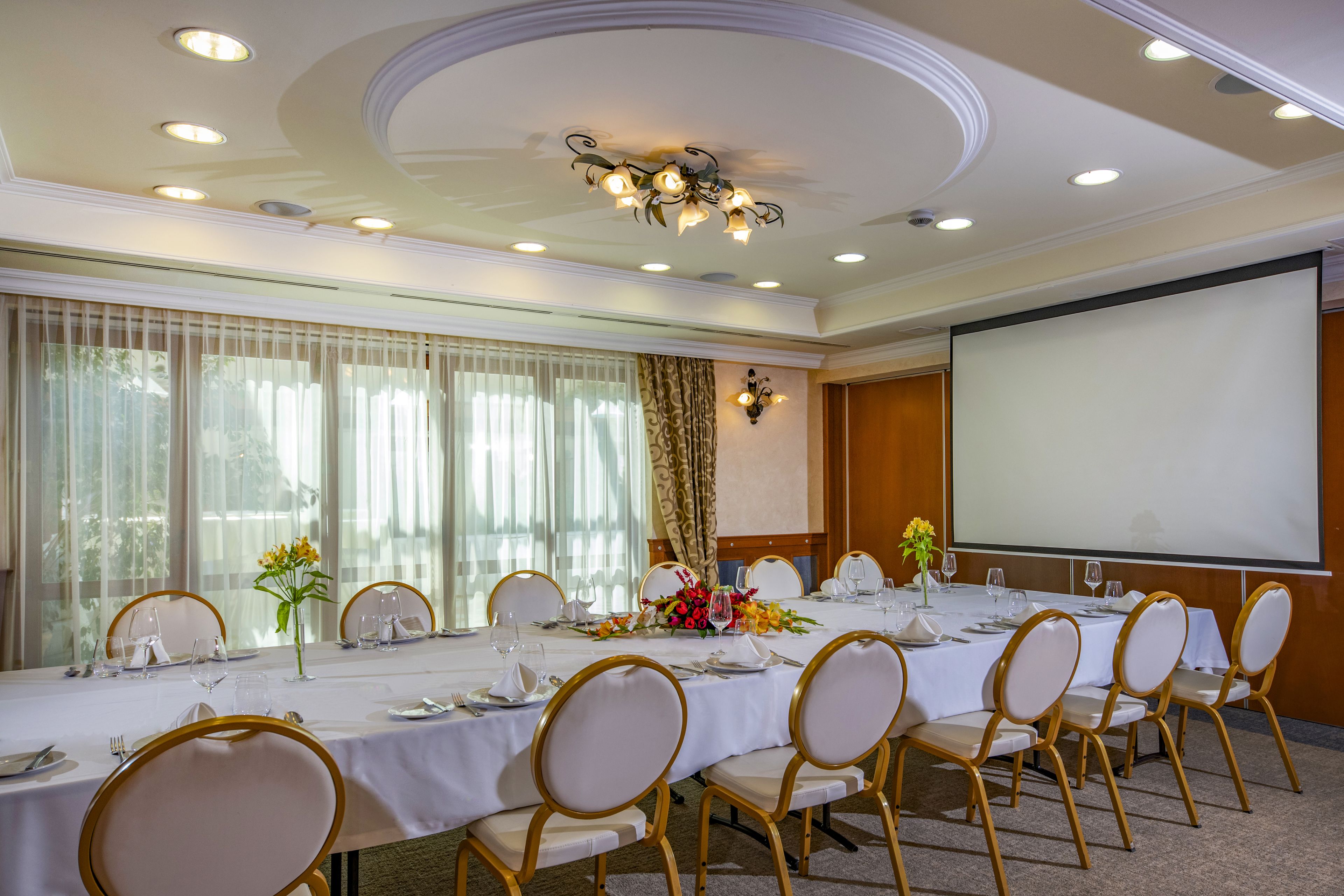 A conference room with a long table, chairs, a projector screen, and a floral centerpiece.