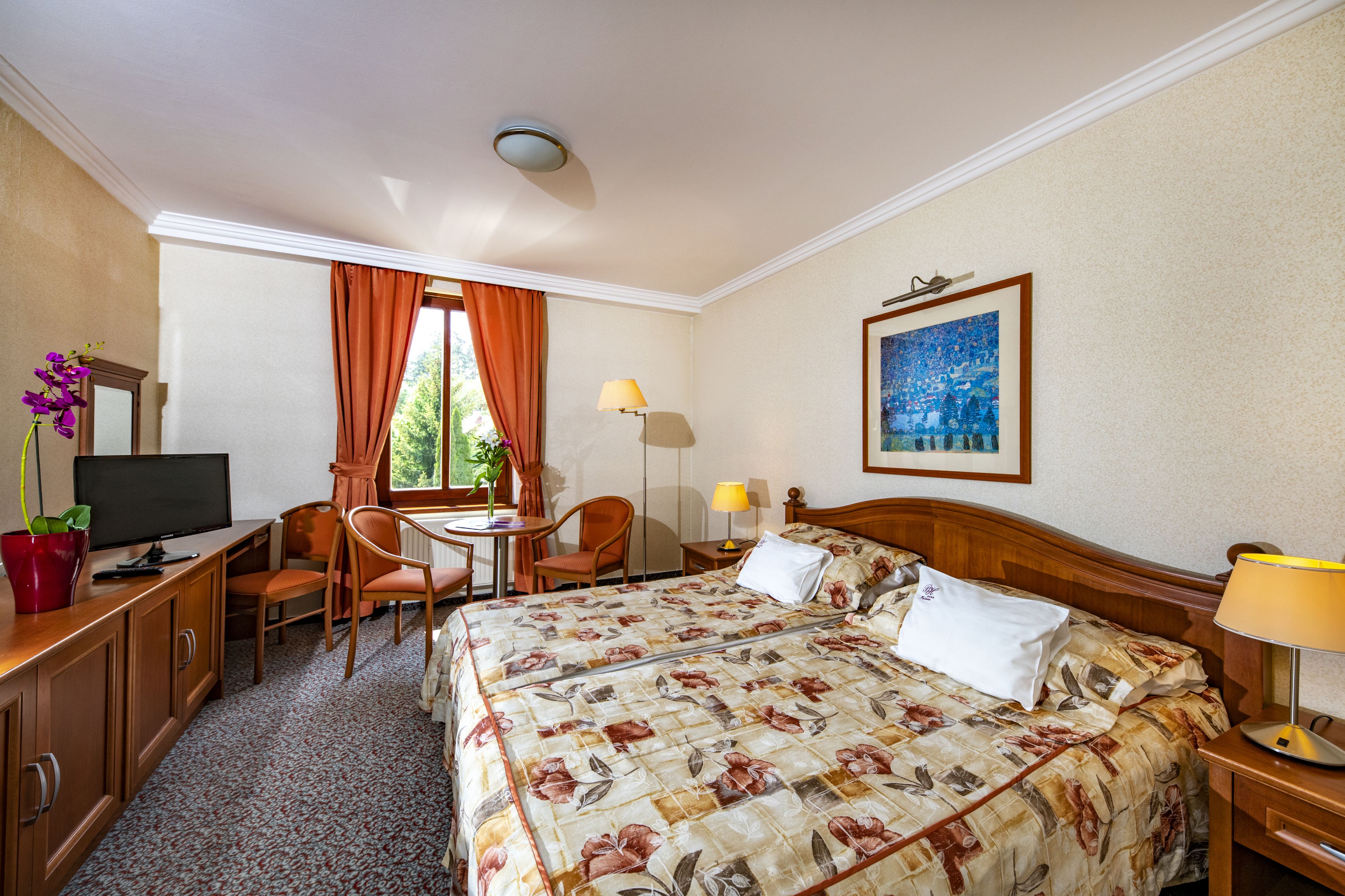 A hotel room with a bed, desk, chair, TV, and a window with curtains.