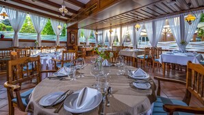 Un restaurante con mesas dispuestas para comer, sillas de madera y amplias ventanas con cortinas.