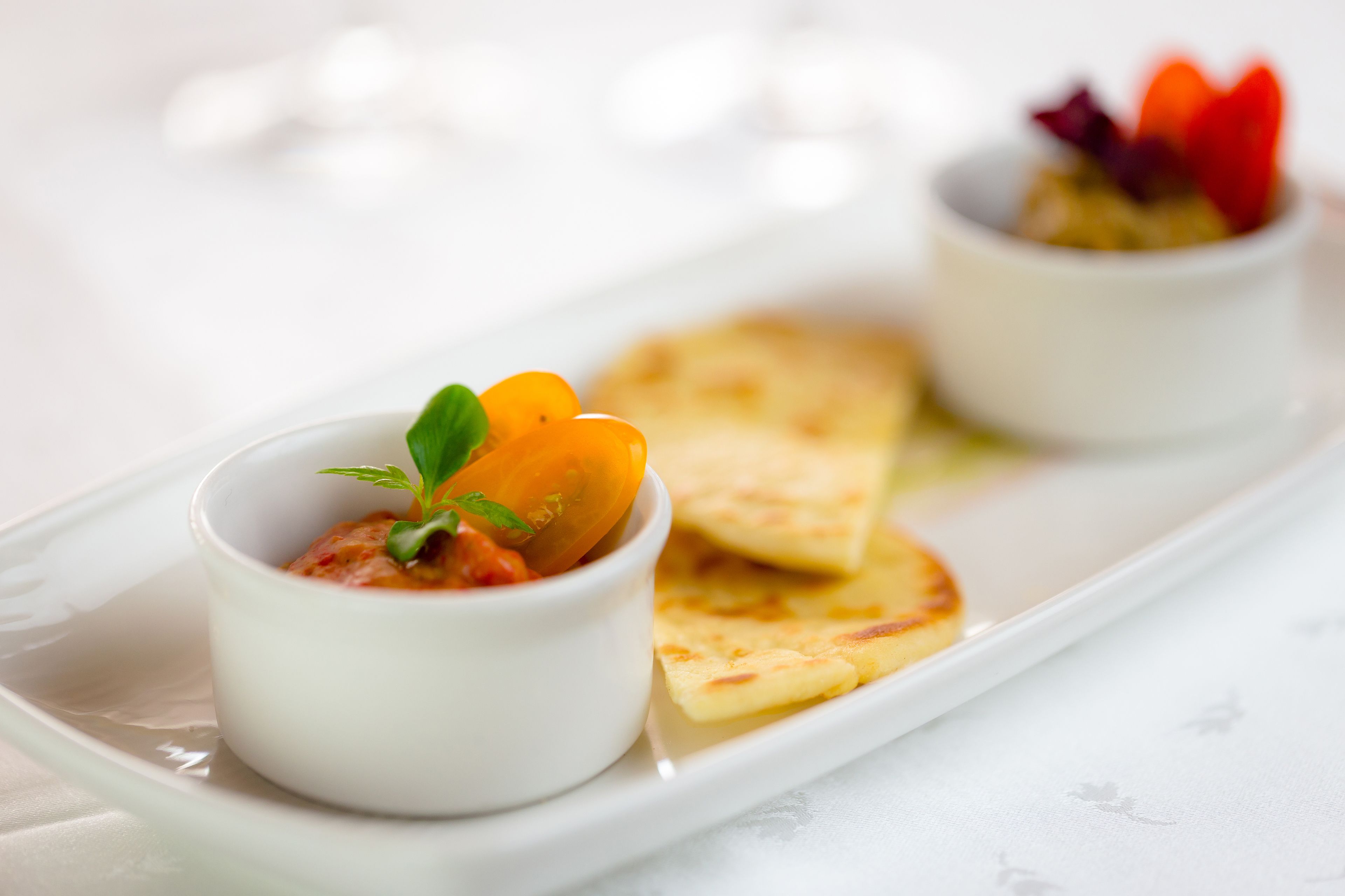 A white plate with two small bowls of food and a piece of flatbread.