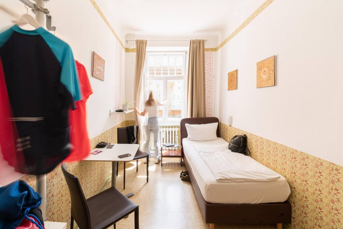A compact hotel room with a single bed, a small desk, a chair, and a wardrobe.