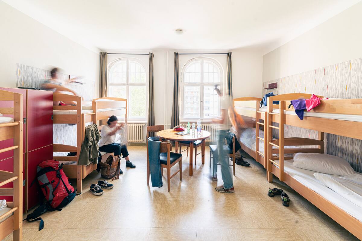 A dormitory room with bunk beds, a round table, and chairs.