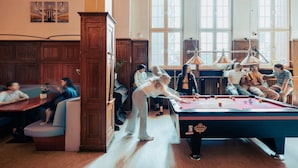 Une table de billard dans une pièce aux murs lambrés et aux grandes fenêtres.
