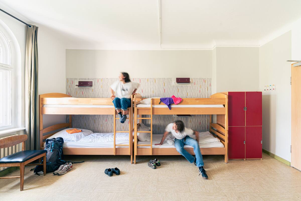 A dormitory room with bunk beds, a wooden wardrobe, and a bench.