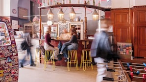 Un espace bar avec des tabourets, un baby-foot et un panneau lumineux au néon.