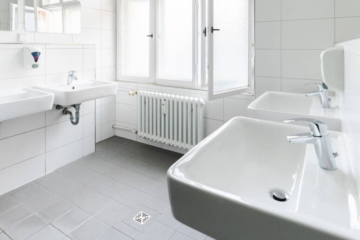A modern bathroom with white fixtures, a large arched window, and a radiator.