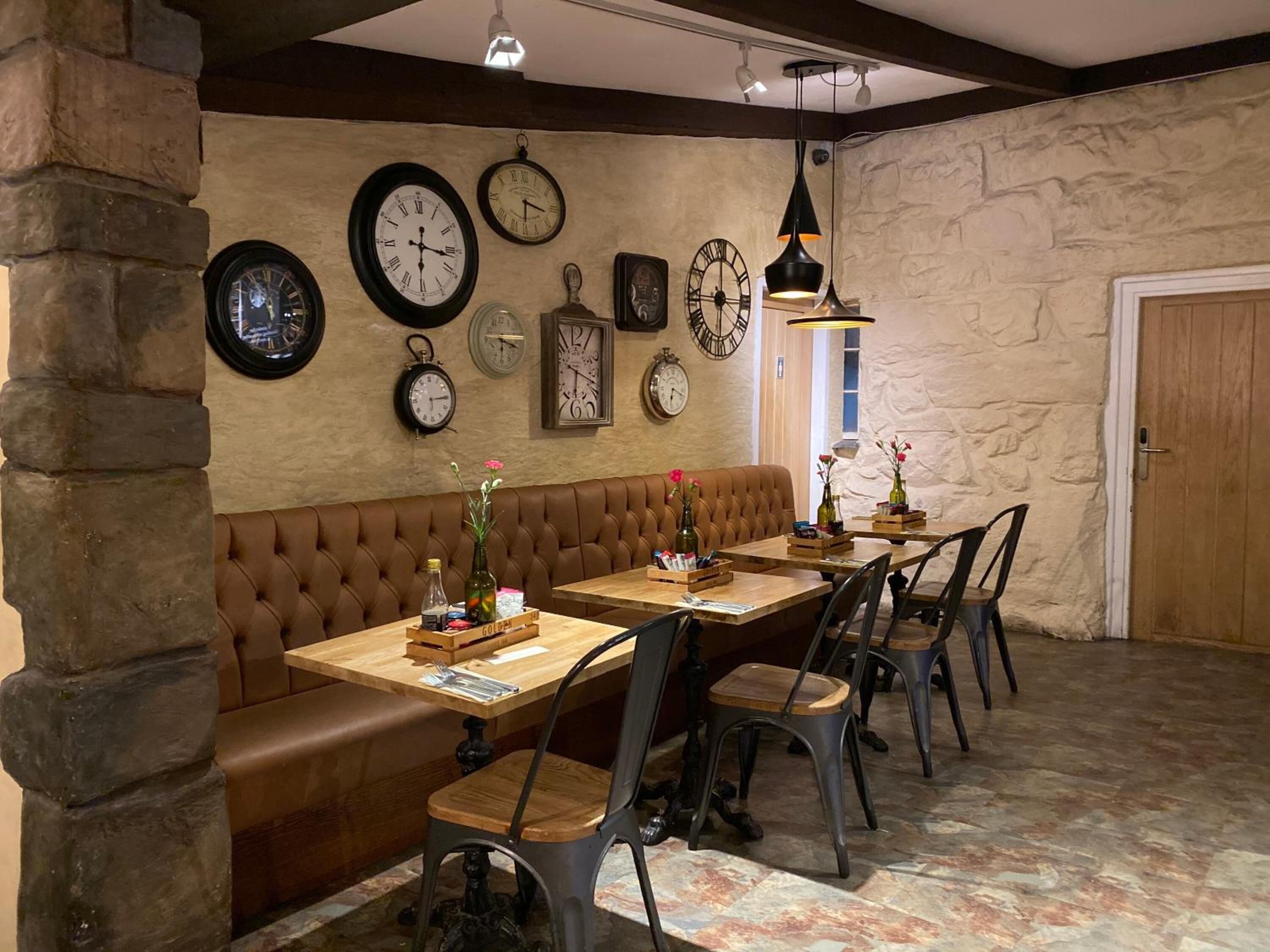 Un coin repas chaleureux avec un banc en cuir marron, des tables en bois et des chaises en métal.
